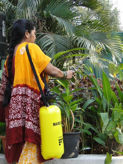 Woman in a yellow and red traditional outfit using a yellow MARS spraying can on plants.